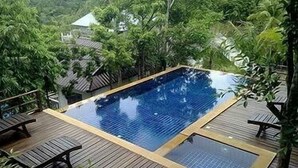 Ein rechteckiger Pool im Freien mit einer Holzterrasse, vor einer Kulisse aus üppiger Vegetation und einem Hügel.
