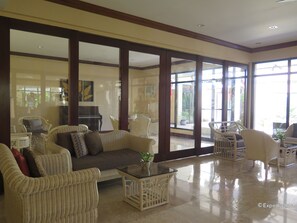 Amplia sala de estar con mobiliario de mimbre, una mesa de centro de vidrio y grandes ventanales con vistas al exterior.