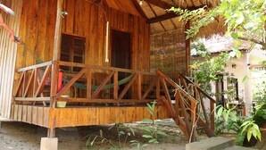 A wooden cabin with a porch, a hammock, and a thatched roof. - Bird of Paradise Bungalows (Kep)