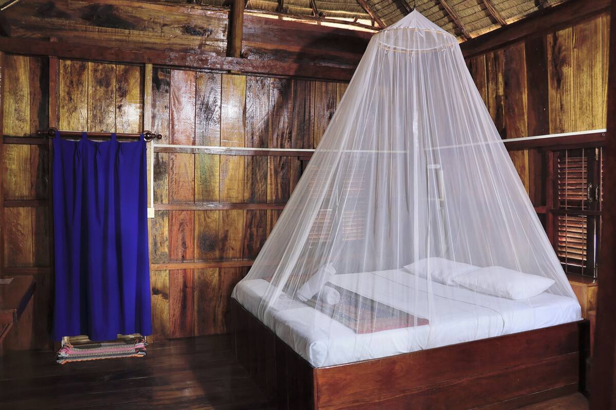 A wooden room with a bed under a mosquito net.