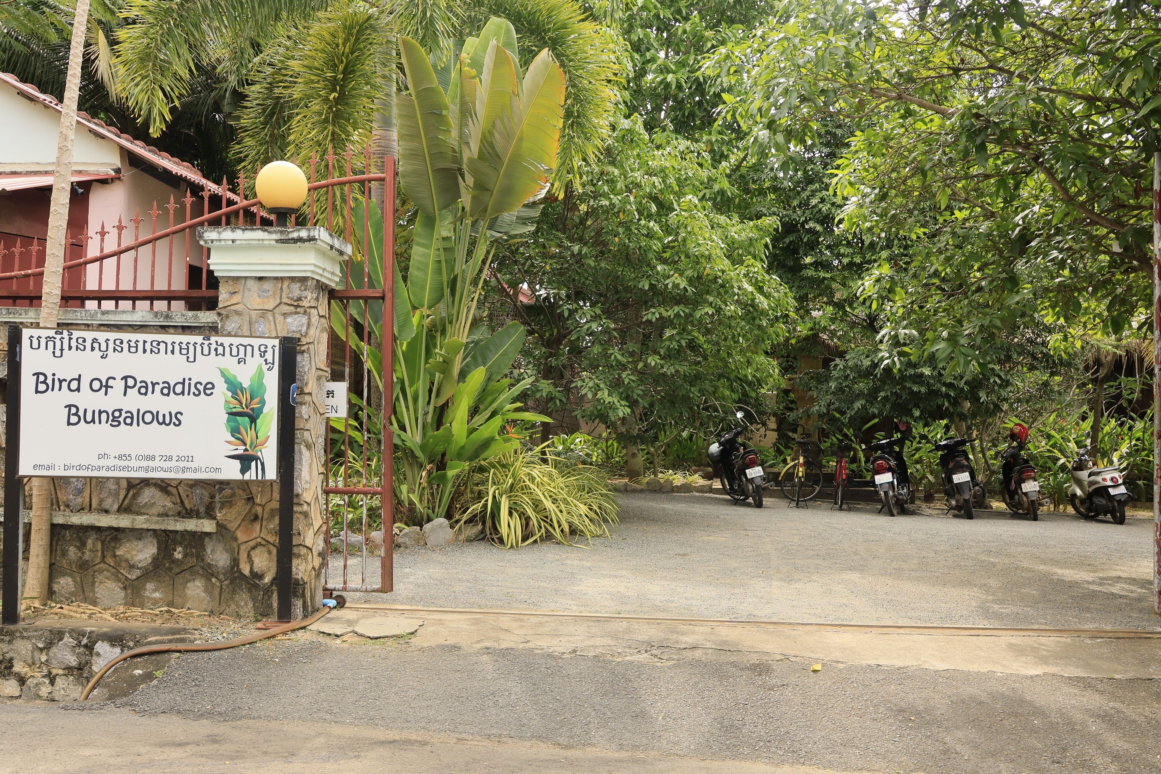 A sign for Bird of Paradise Bungalows with a stone base and a decorative ball on top.
