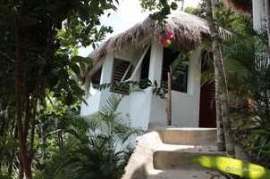 A house with a thatched roof, surrounded by lush greenery and palm trees.