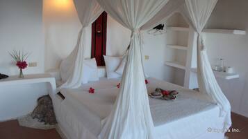 Un dormitorio con cama con dosel, ropa de cama blanca, una mesita de noche con un jarrón de flores y una pared de acento roja.