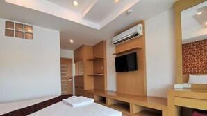 A modern hotel room with a bed, built-in wardrobe, TV, and air conditioning unit.