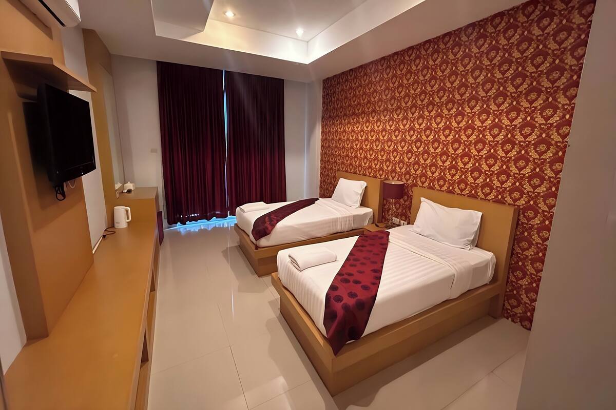 A hotel room with two beds, a flat-screen TV, a bench, and a patterned wall.