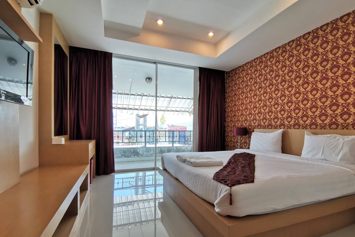 A modern hotel room with a large bed, a TV, and a balcony with a view.