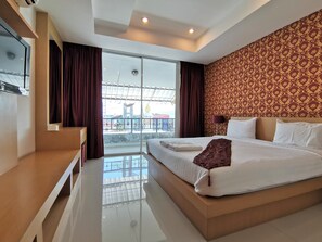 A modern hotel room with a large bed, a TV, and a balcony with a view. - Le Desir Resortel (Chalong)