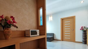 A modern hotel room with a wooden bench, a microwave, a sofa, and a door with a number.