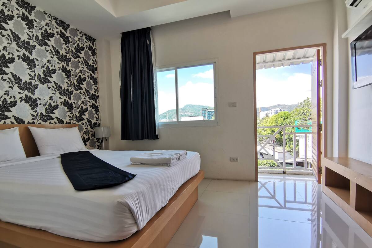 A hotel room with a large bed, a window with a view of the city, and a balcony.