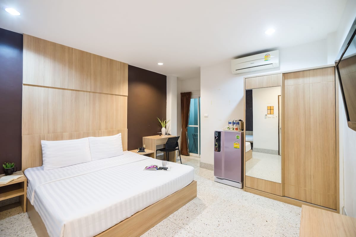A modern hotel room with a large bed, a desk, a refrigerator, and a wardrobe.