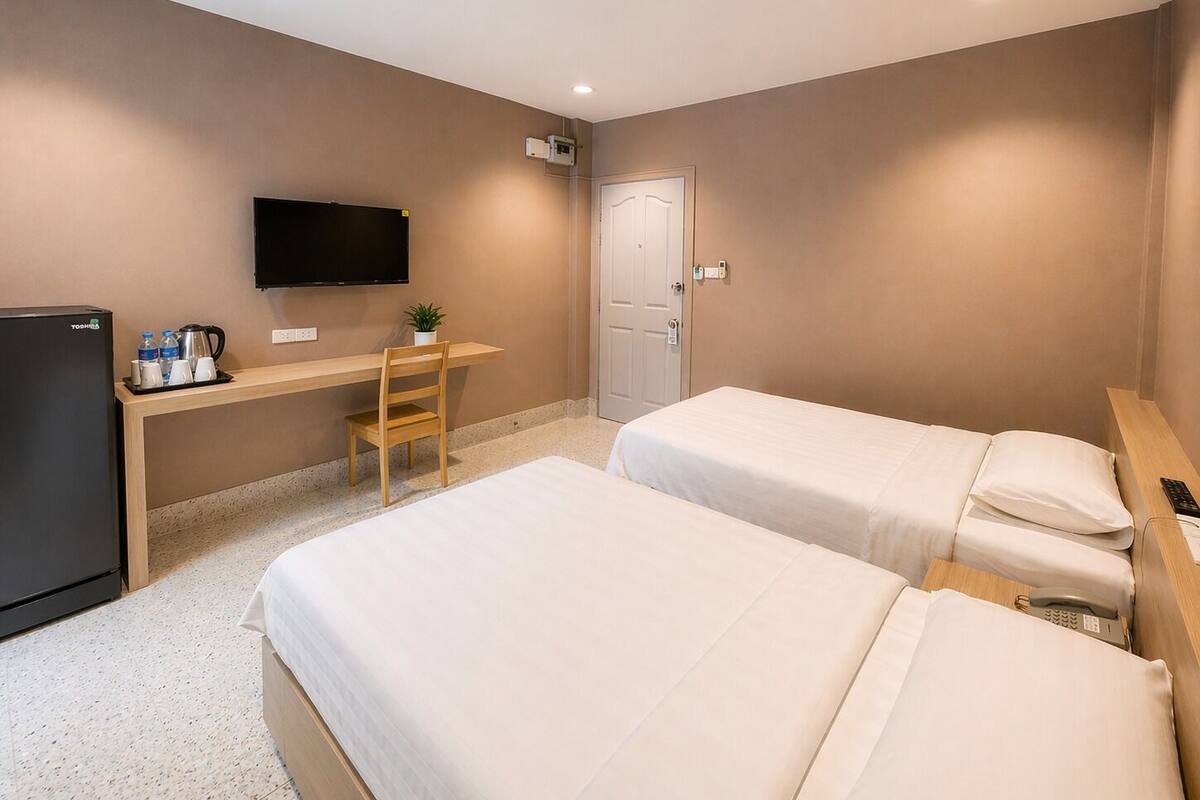 A hotel room with two beds, a desk, a TV, a refrigerator, and a door.
