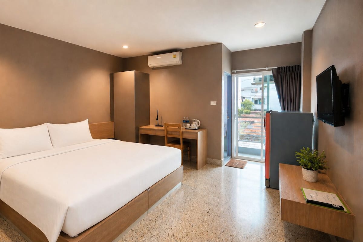 A hotel room with a bed, desk, chair, TV, and a potted plant.