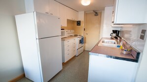 A compact kitchen with white cabinets, a refrigerator, a microwave, an oven, and a sink. - Glacier View Condo Suites (Whittier)