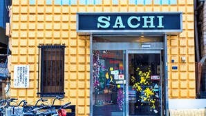Un edificio con fachada de ladrillo amarillo y un letrero que dice "SACHI" sobre la entrada.