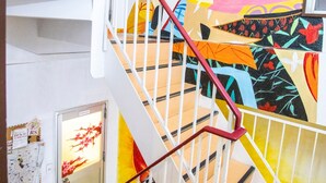 Una escalera con un mural colorido en la pared, barandal blanco y una puerta con un panel de vidrio.