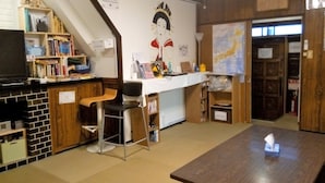 A room with a wooden desk, a chair, a television, and a bookshelf. - Peace House Showa - Hostel (Osaka)
