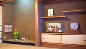 A traditional Japanese room with tatami flooring, a low wooden cabinet, and a small shelf with decorative items. - Peace House Showa - Hostel (Osaka)