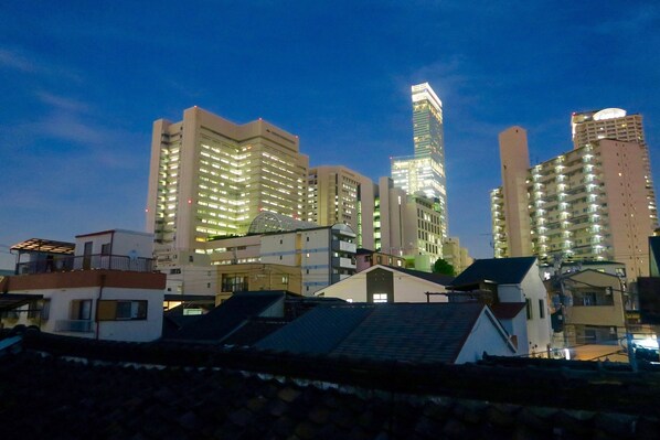 A cityscape at dusk with modern high-rise buildings, including a prominent skyscraper with illuminated windows.