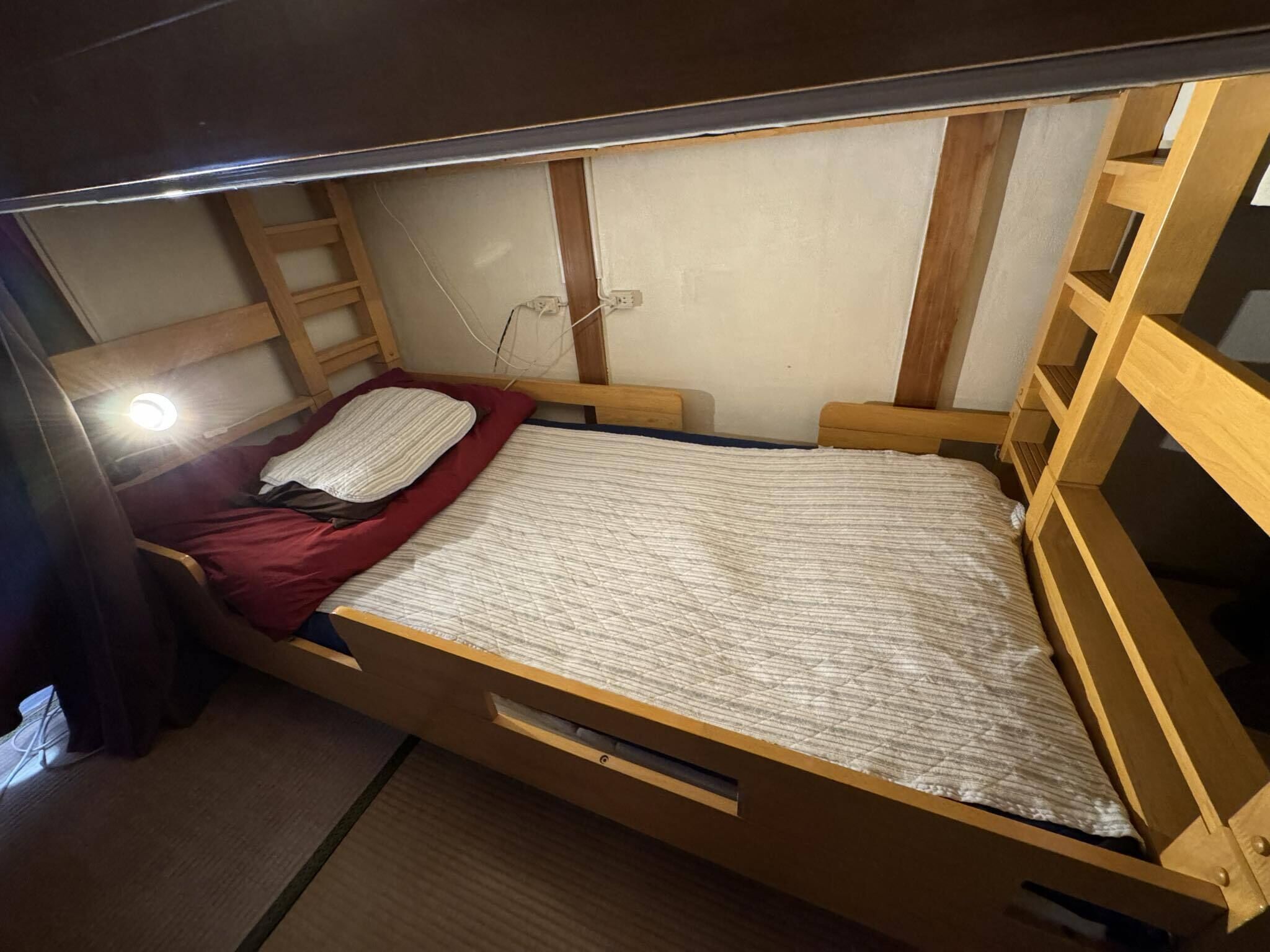 Habitación pequeña con cama individual, estructura de madera, manta roja y colcha blanca.