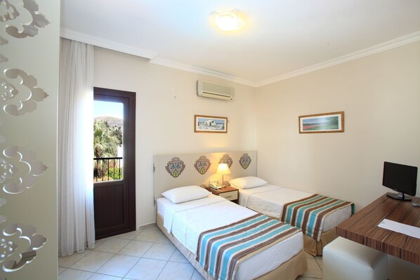 Habitación de hotel con dos camas, un escritorio y un televisor. Cuenta con adornos en la pared y una puerta que ofrece vistas al exterior, con vegetación.