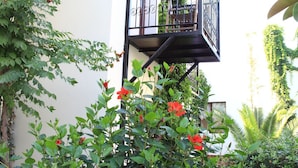 Ein Balkon mit Metallgeländer, umgeben von üppigem Grün und roten Blüten.