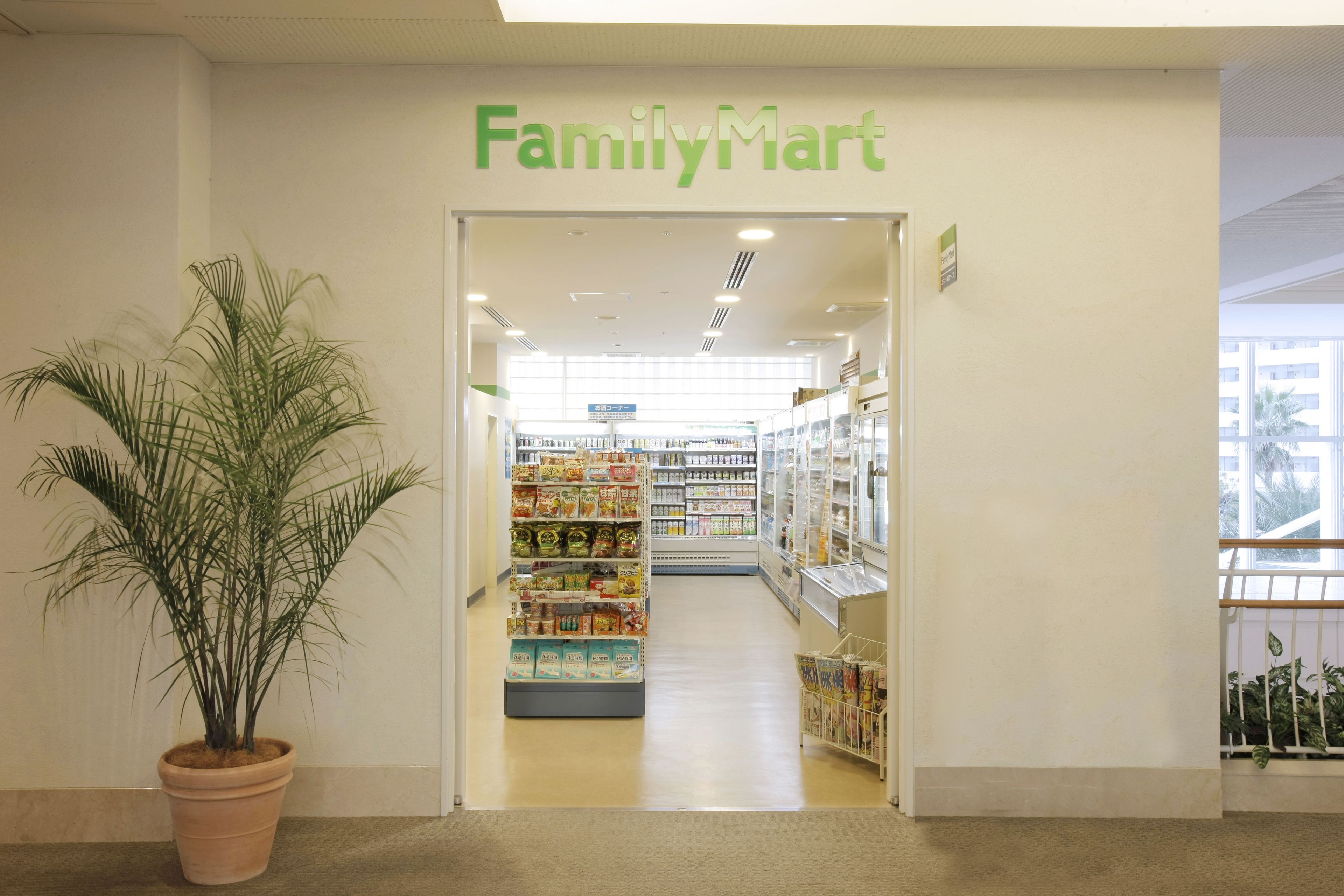 The entrance of a FamilyMart store with a potted plant and shelves stocked with products.