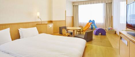 Habitación de hotel con una cama grande, un escritorio, una silla, una mesita y un área de juegos infantil con juguetes y un tobogán.