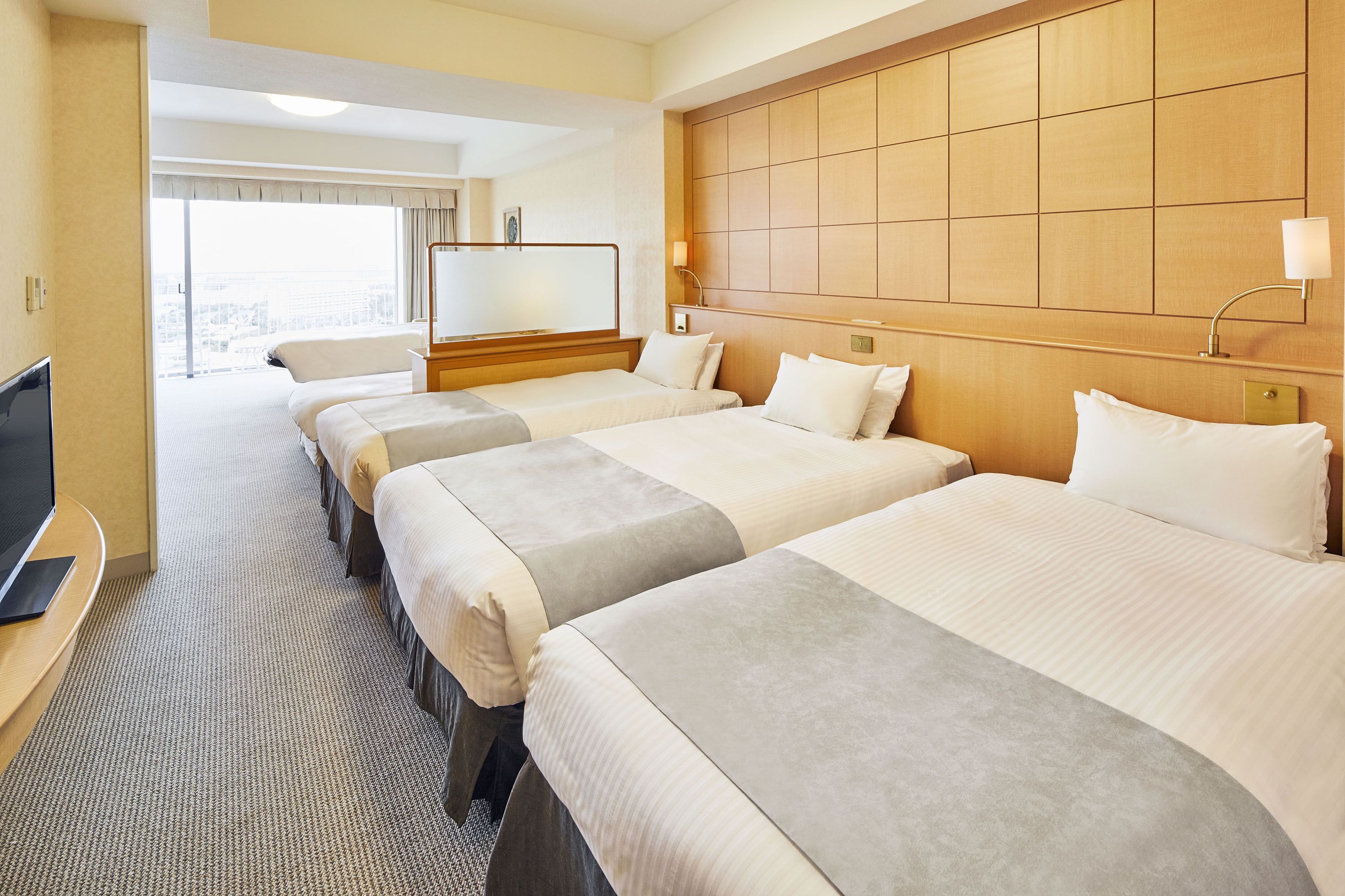 A hotel room with three beds, a TV, and a large window.