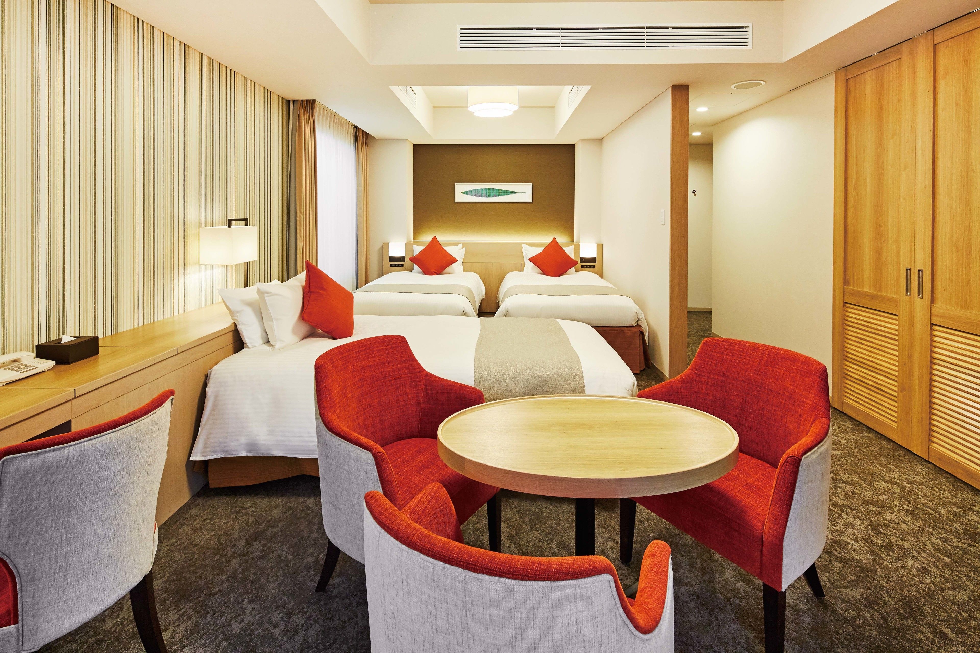 Une chambre d’hôtel avec deux lits, un bureau, une chaise, une table ronde et une armoire.