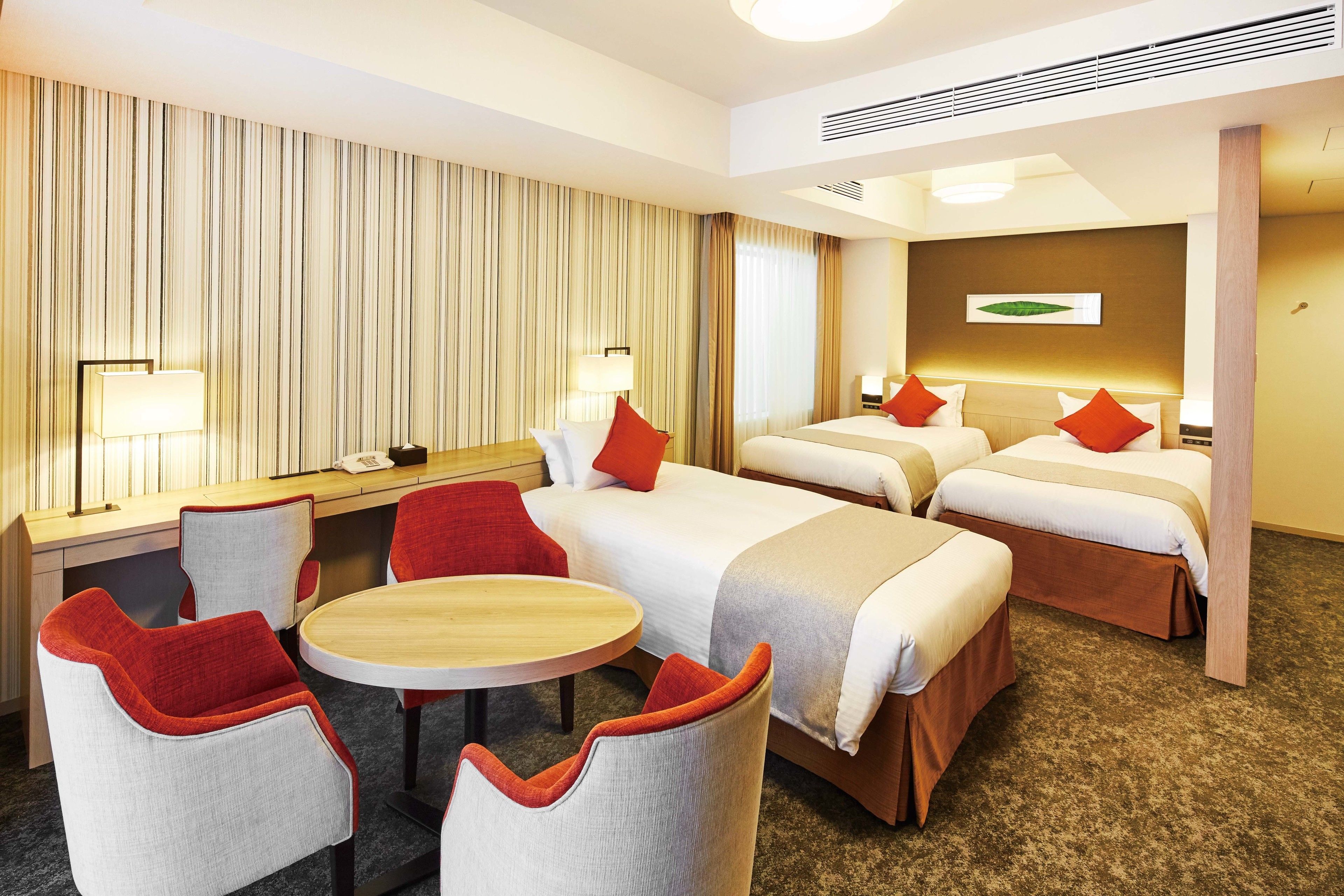 A hotel room with two beds, a desk, and a round table.