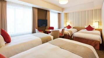 A hotel room with three beds, a TV, a desk, and a chair.