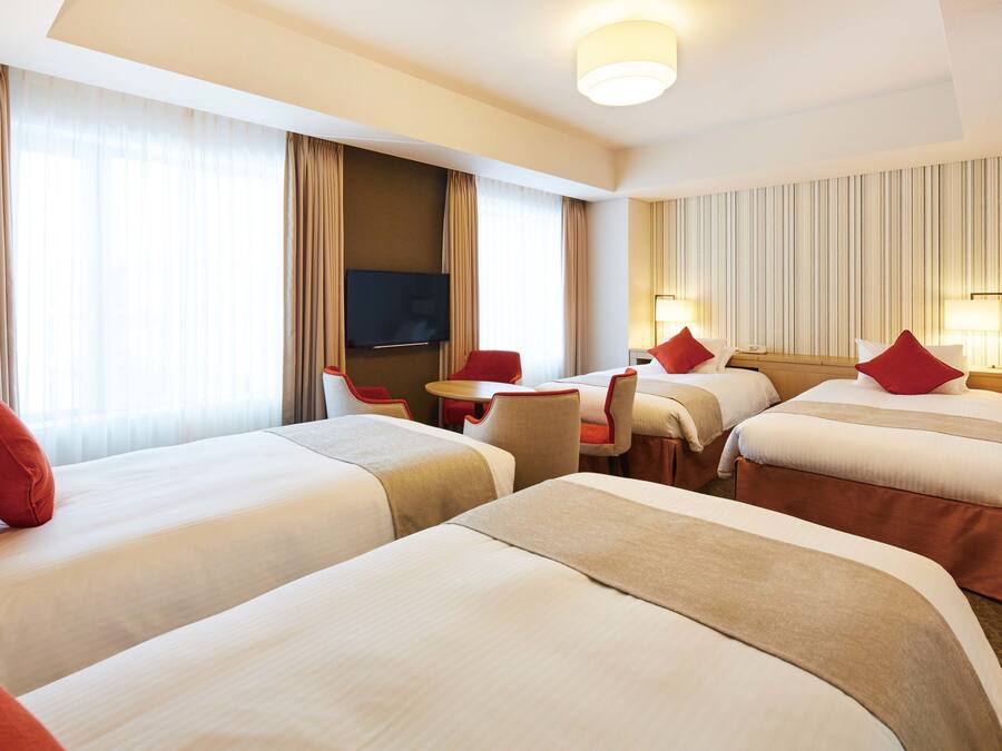 A hotel room with three beds, a TV, a desk, and a chair.