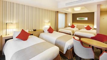 A hotel room with three beds, a small table, and two chairs.