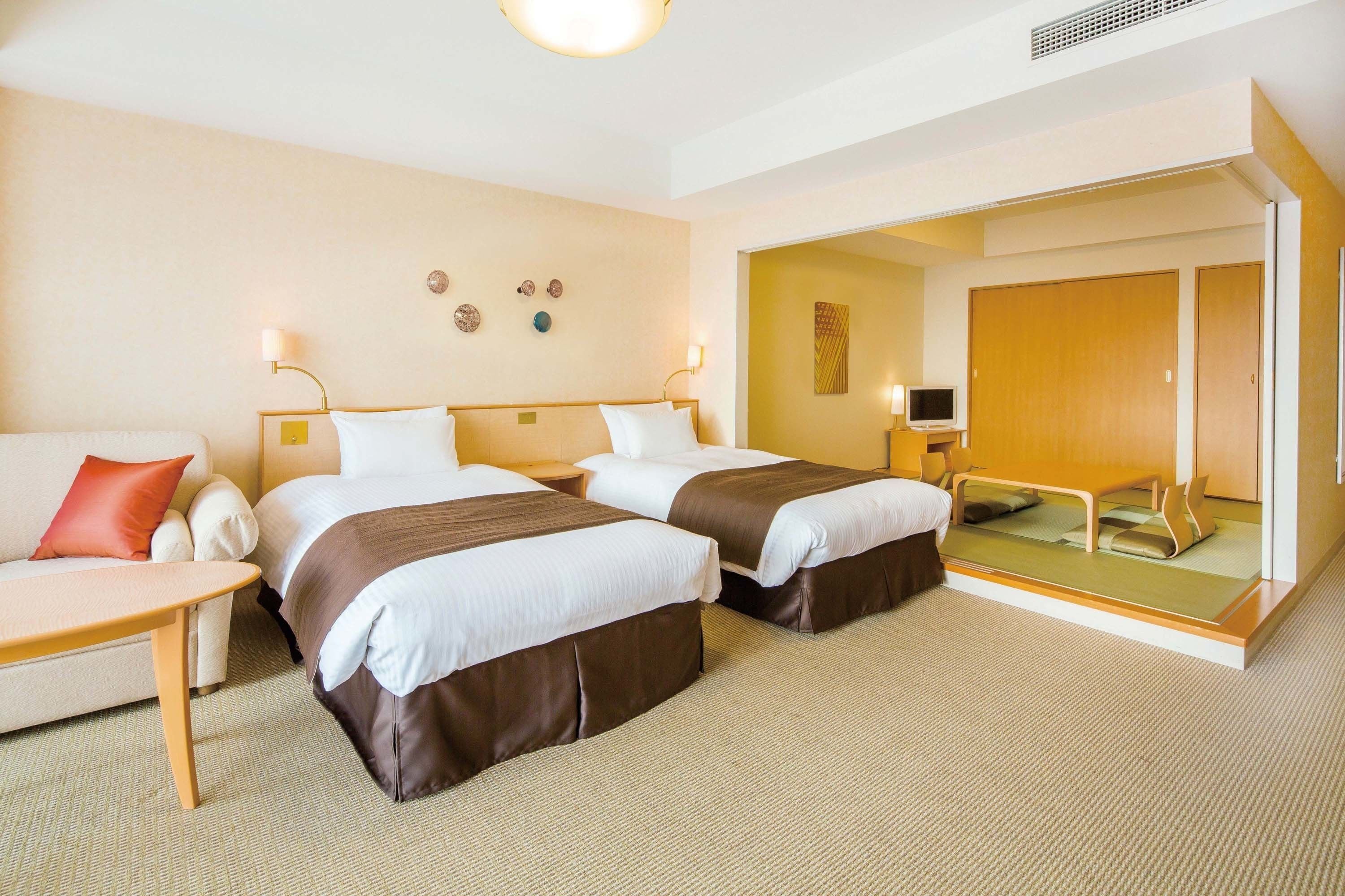 A hotel room with two beds, a sofa, a small table, and a mirror.
