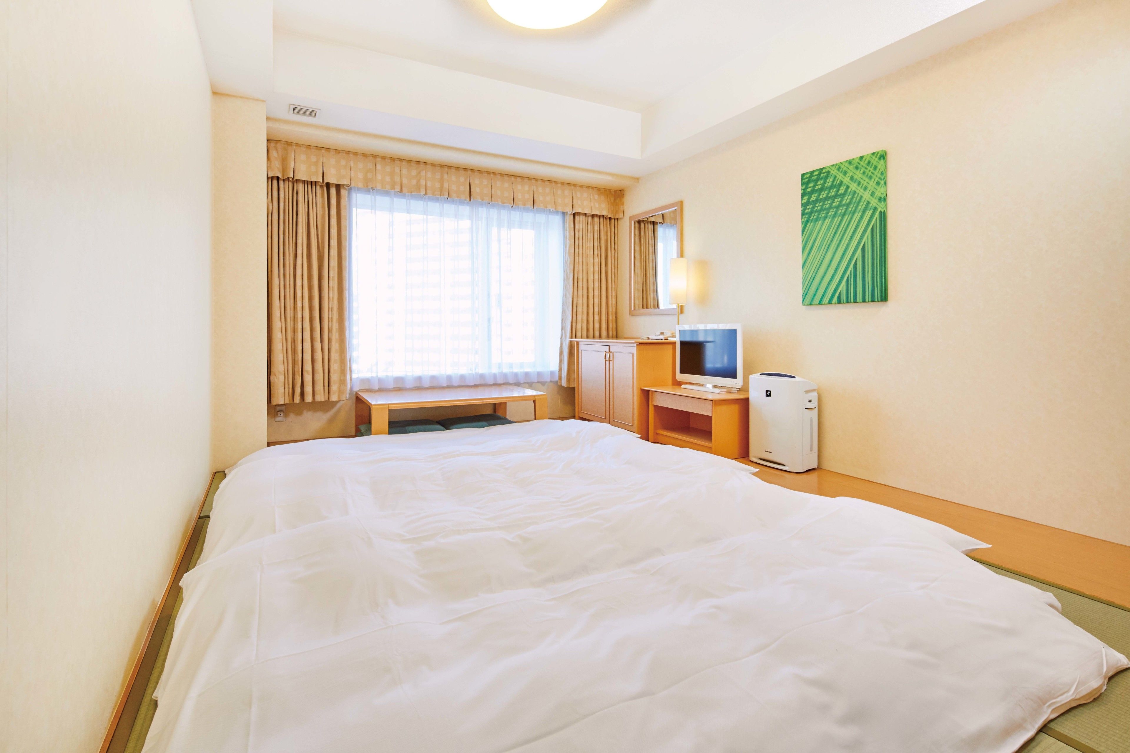 A hotel room with a large bed, a desk with a computer, a TV, and a green abstract painting on the wall.