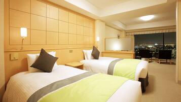 A hotel room with two beds, a nightstand, a desk, and a large window with a city view.