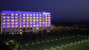 A hotel with multiple floors, a well-lit facade, and a landscaped garden area. - Denissons (Hubli)