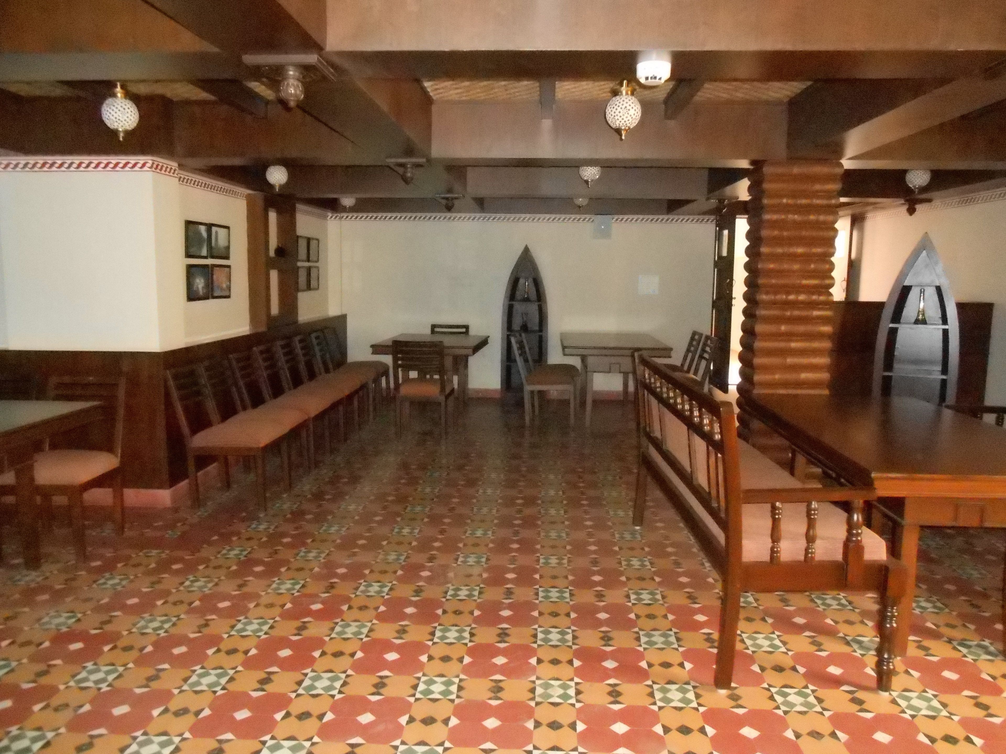A dining area with wooden benches and tables, patterned floor tiles, and a vaulted ceiling with exposed beams.