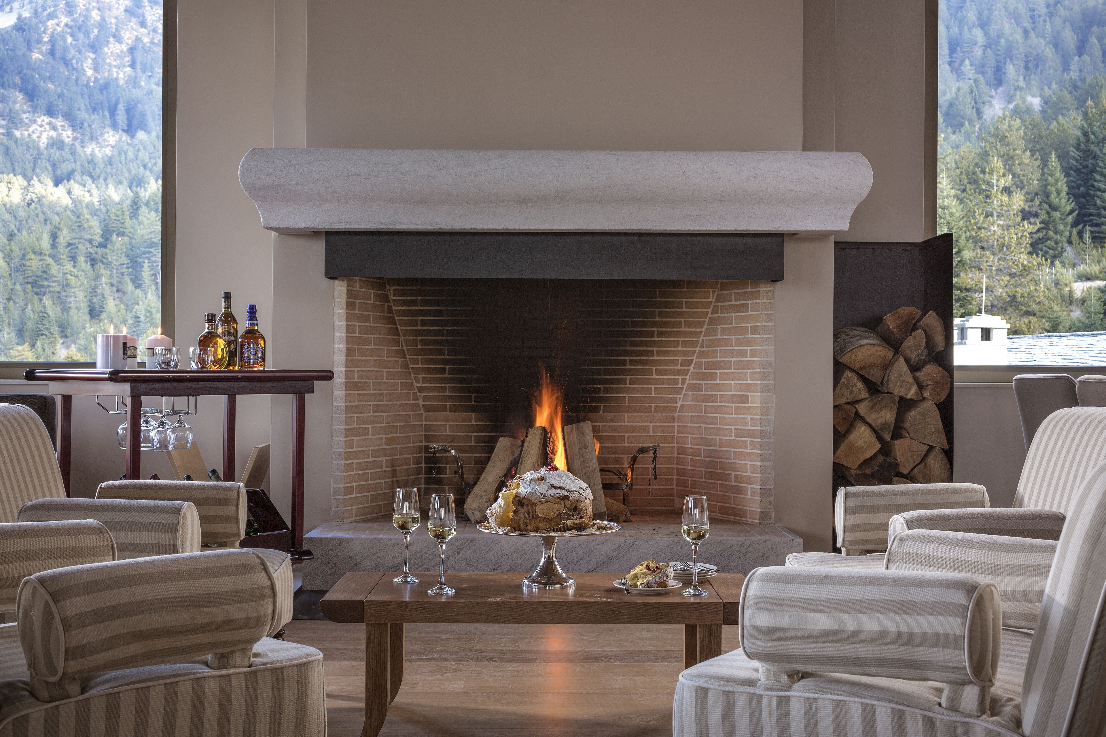 A cozy room with a fireplace, striped chairs, a table with a cake and glasses, and a mountain view.