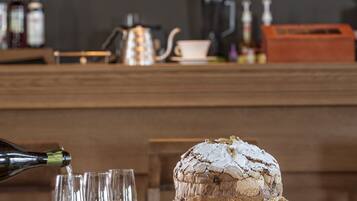 A bar area with a cake on a glass stand, three glasses of white wine, and a bottle of champagne being poured.