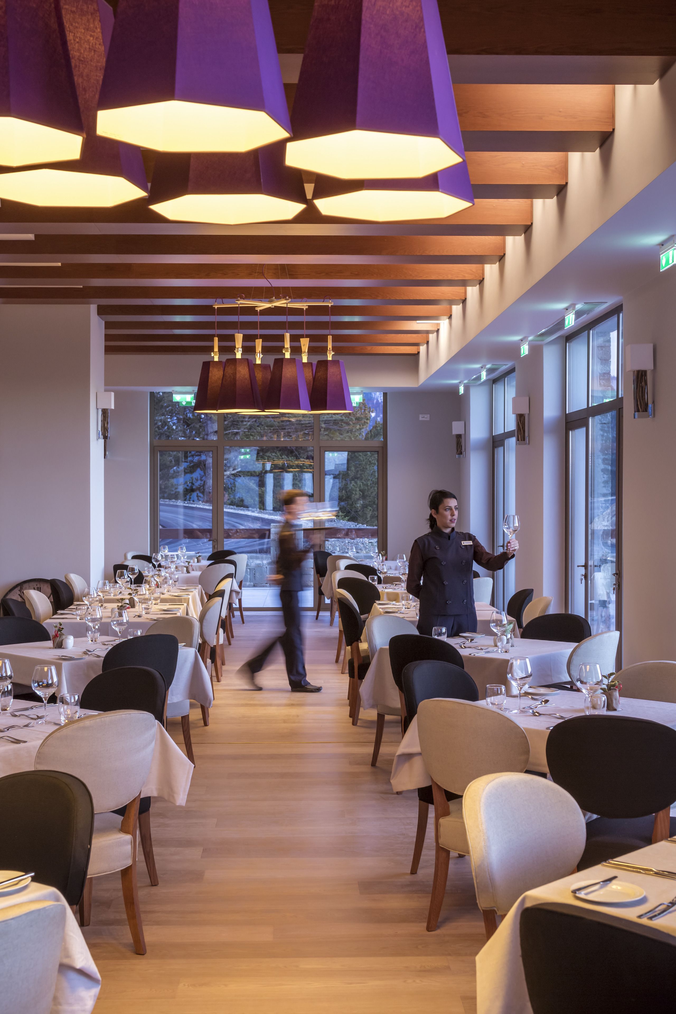 Un espace de restauration moderne, avec des tables dressées pour le service, de grandes fenêtres et des luminaires contemporains.