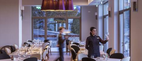 Un espace de restauration moderne, avec des tables dressées pour le service, de grandes fenêtres et des luminaires contemporains.