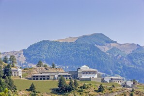 A mountainous landscape with several buildings, including a large white structure and a smaller building with a sloped roof, surrounded by greenery and trees. - Grand Forest Metsovo (Metsovo)