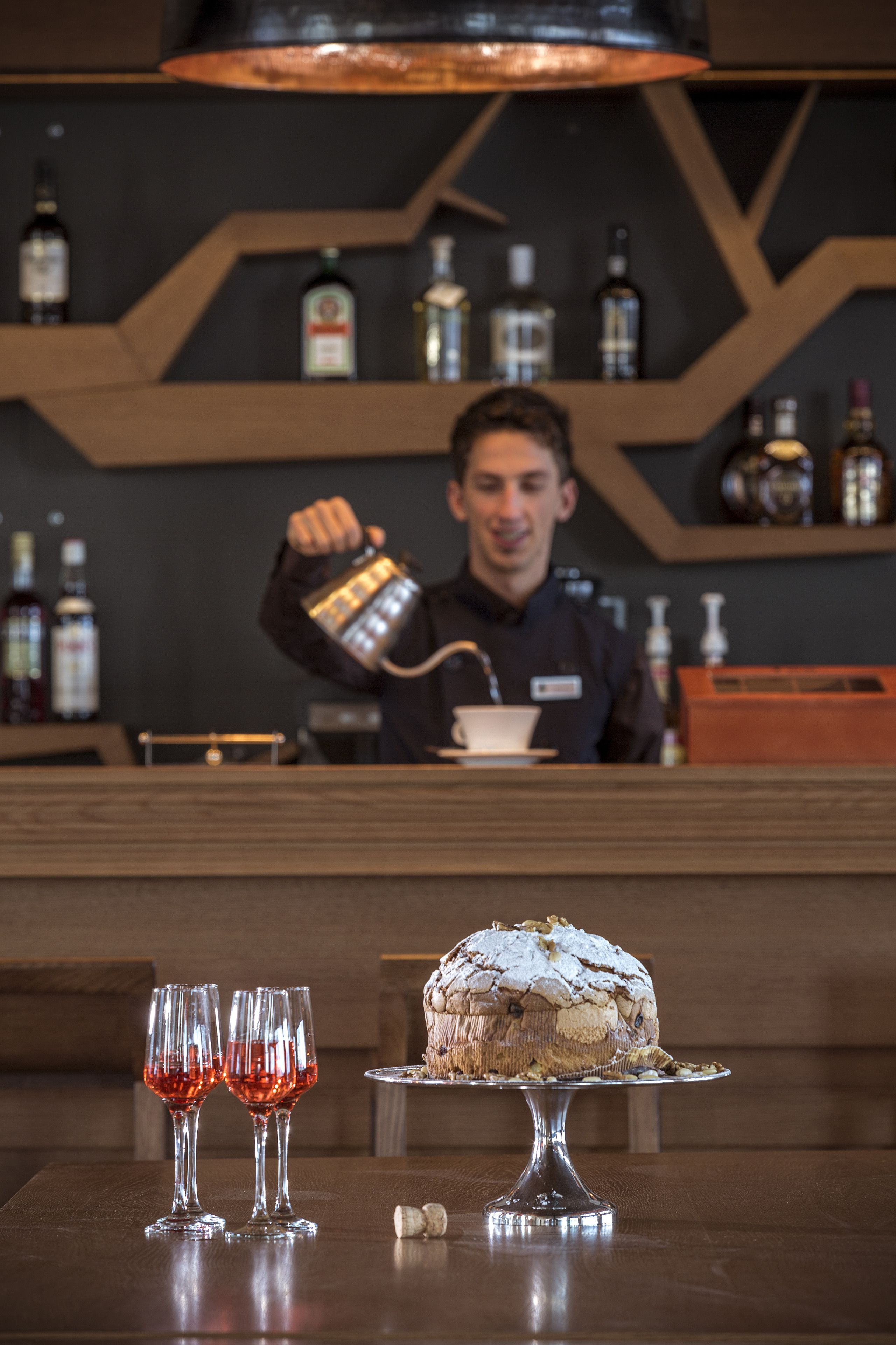 Eine Bar mit einem Barkeeper, der ein Getränk einschenkt, zwei Gläsern Rotwein und einer Torte auf einem Sockel.