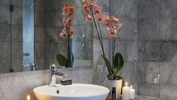 A modern bathroom with a large mirror, a white sink, and two potted orchids.