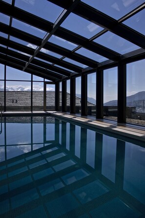 A large indoor swimming pool with clear glass walls, offering views of a mountainous landscape. - Grand Forest Metsovo (Metsovo)