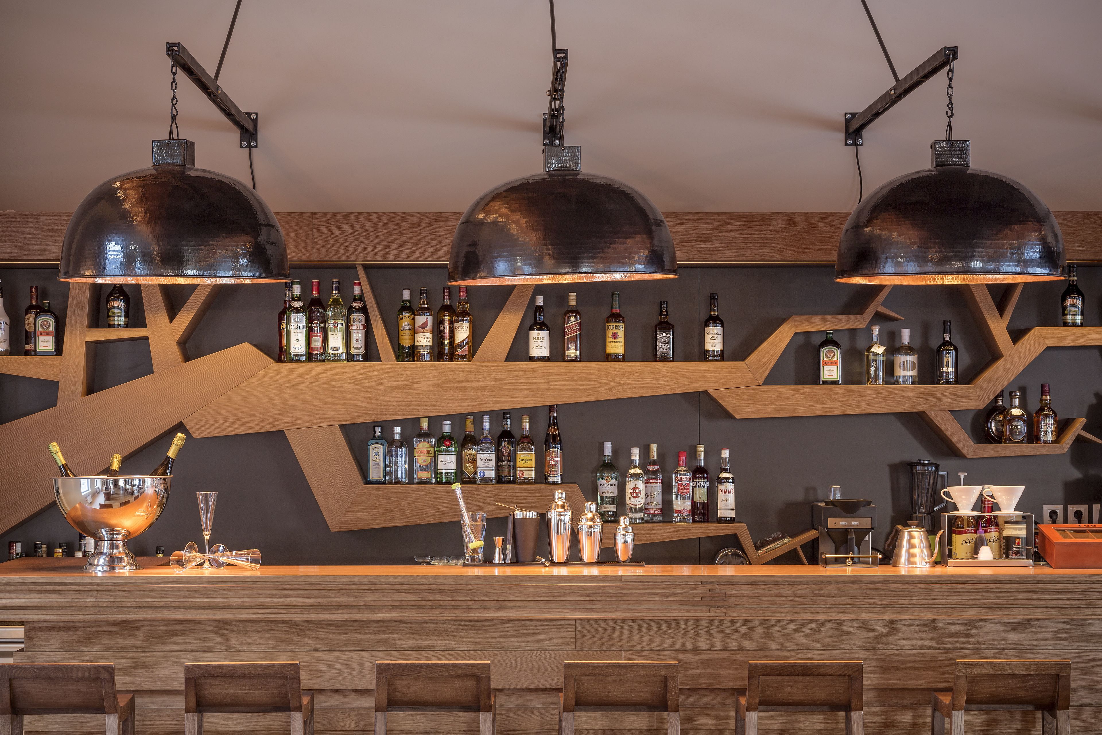A bar area with three large metal lamps, a variety of liquor bottles on shelves, and bar stools.
