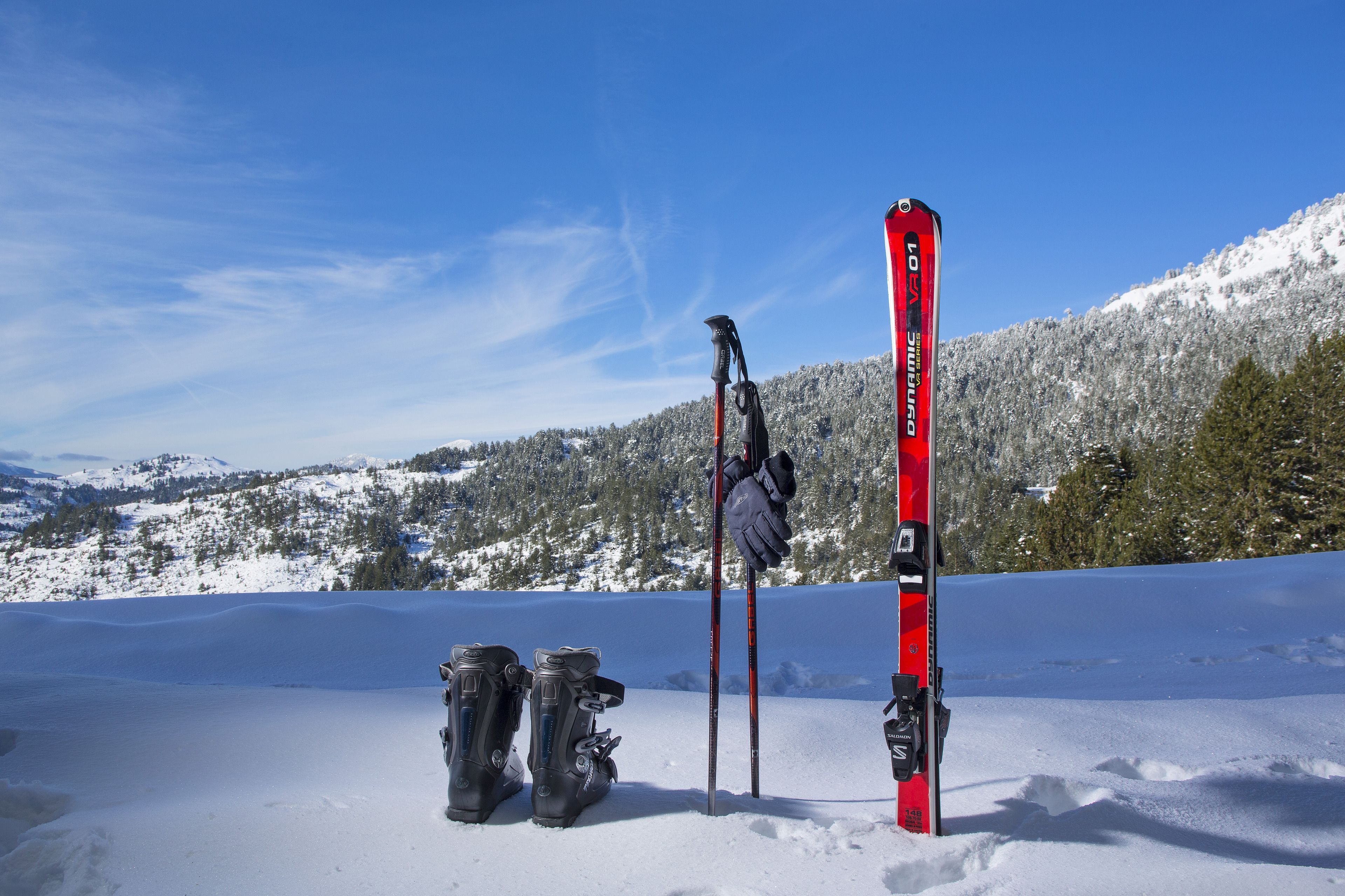 A pair of skis and ski poles leaning against a red ski on a snowy mountain.