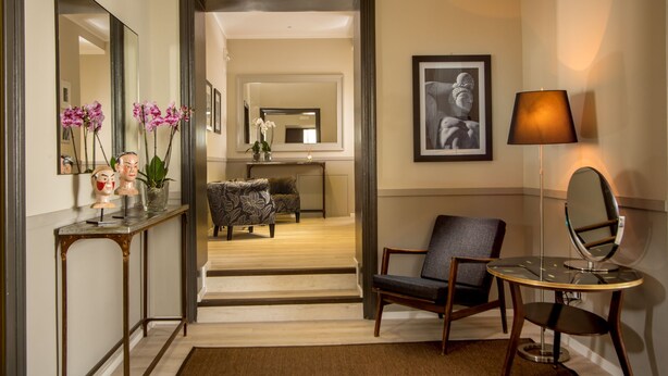 Un hall d’hôtel comprenant un comptoir d’accueil, un espace détente avec un canapé et des fauteuils, un escalier menant à une autre pièce, ainsi qu’une petite table avec une lampe et un miroir.