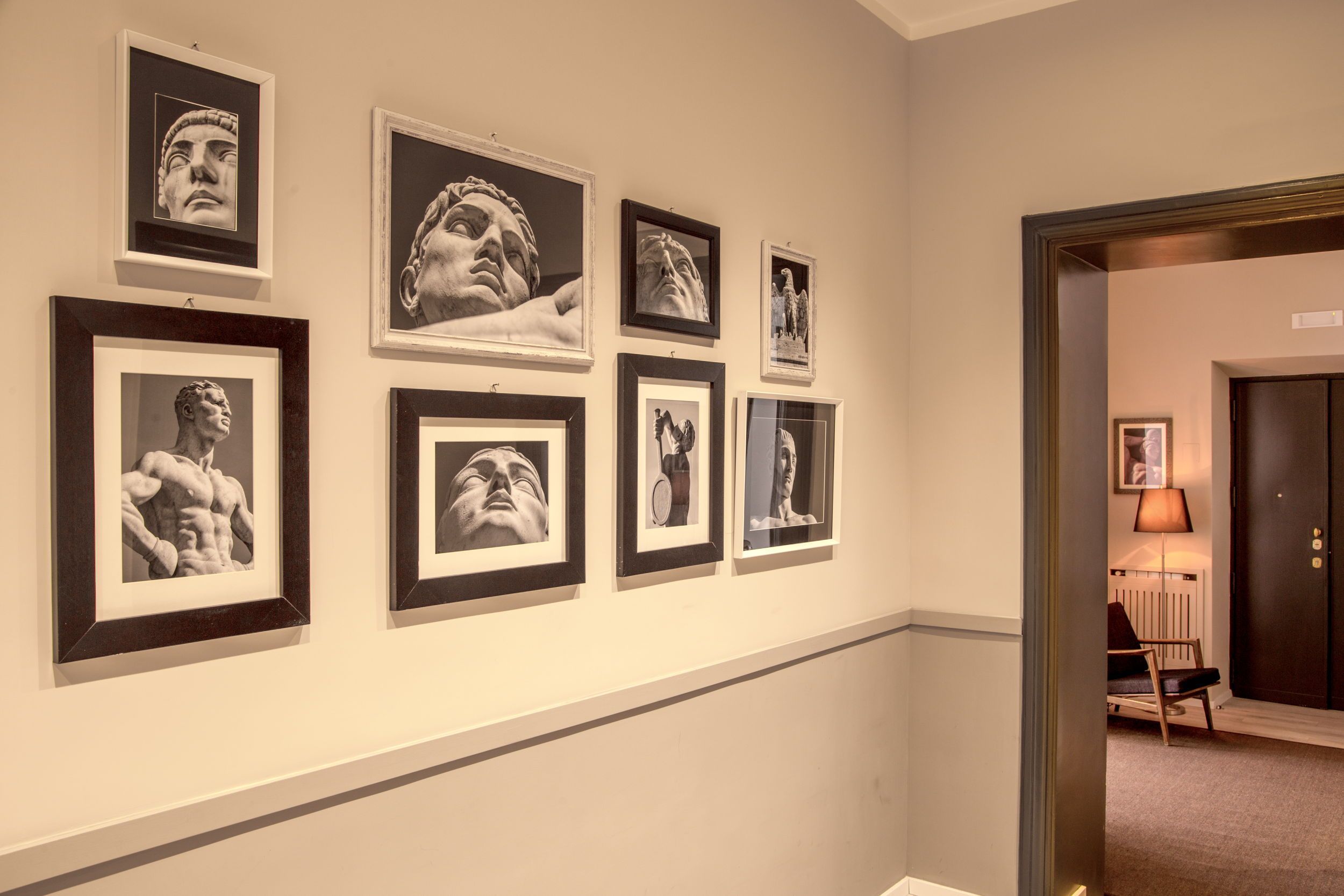 A hallway with framed artwork on the walls, a door, and a chair with a lamp.